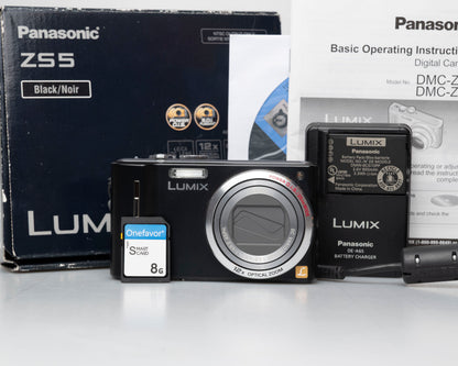 Panasonic Lumix DMC-ZS5 camera with packaging, battery, and memory card